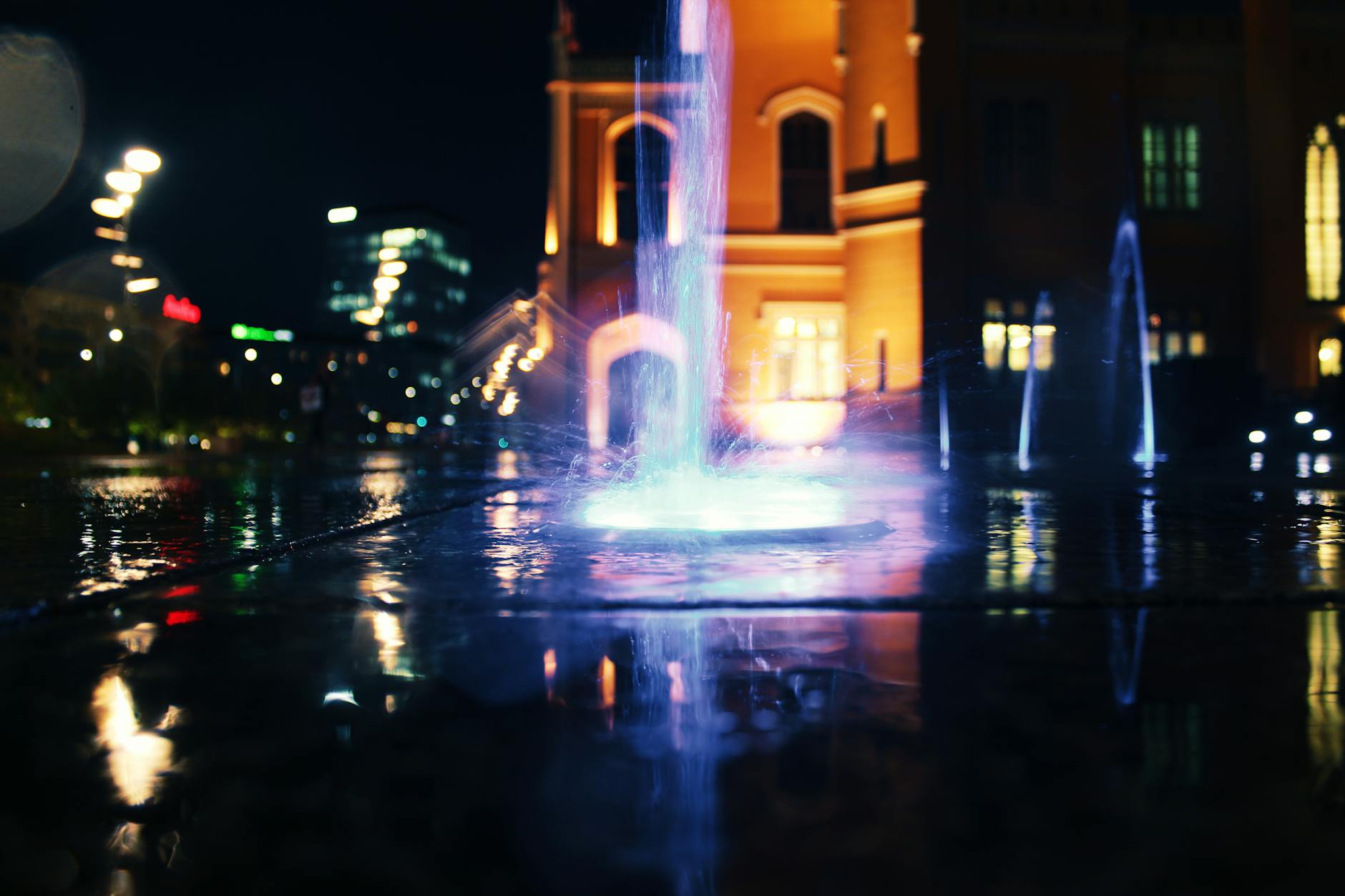 Illuminated water fountain at night with city lights