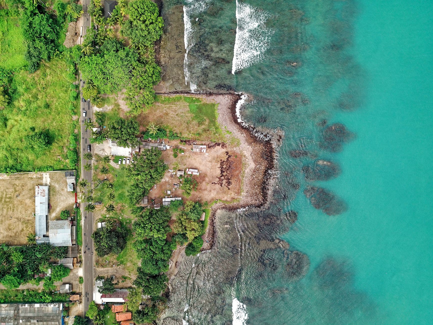 Aerial view of the Anyer coastline in Banten with green water over reef and houses along the shore, the closest Anyer beach day trip from Jakarta