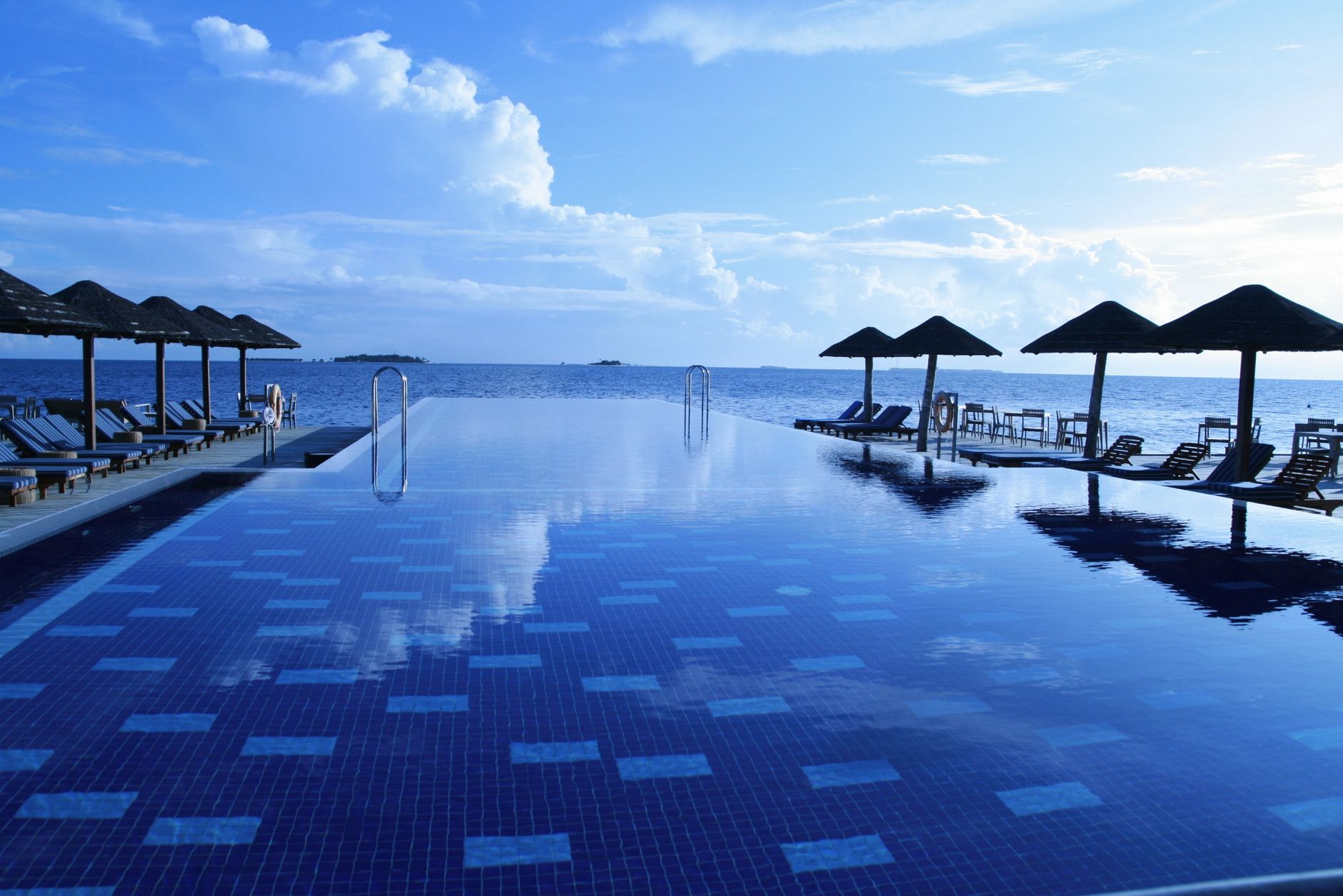 An infinity pool with sun loungers and parasols facing calm open sea at a beach resort