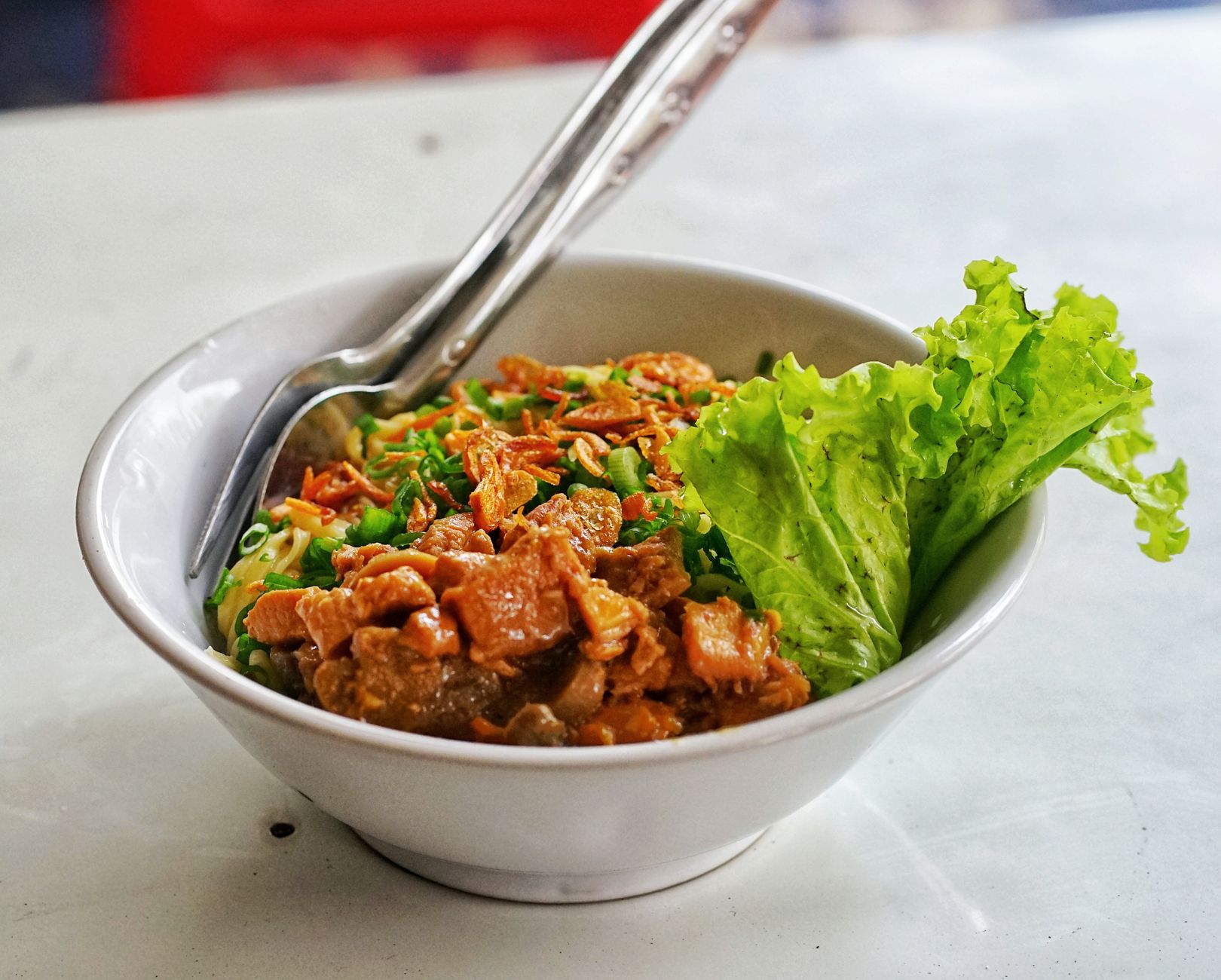 A bowl of Indonesian noodles with shredded chicken and lettuce