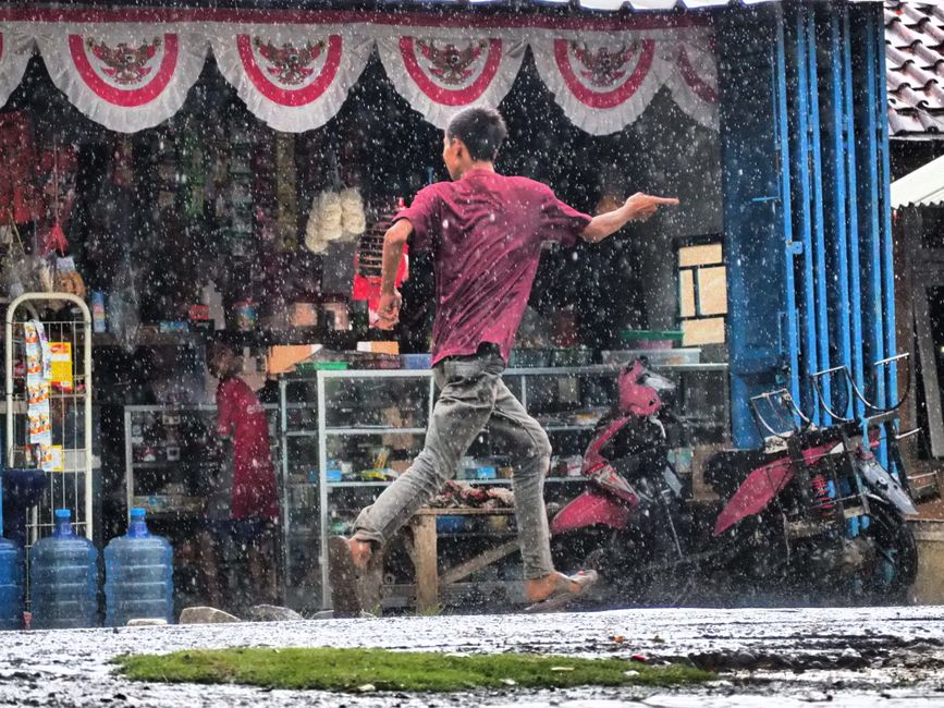 A pedestrian running through a sudden tropical downpour past a roadside shop in Jakarta