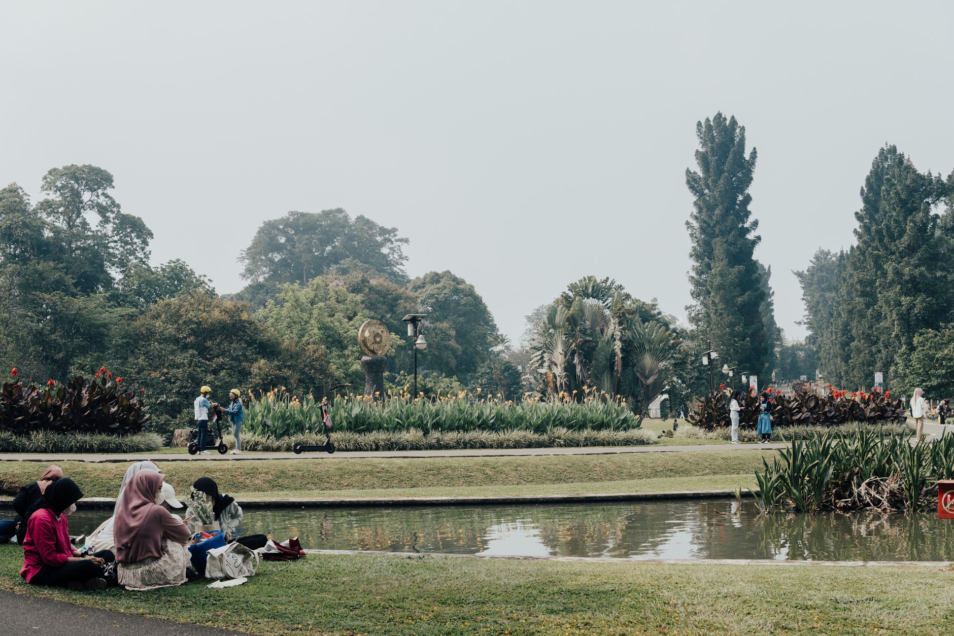 Visitors sitting on the lawns beside the main pond in Kebun Raya Bogor, the highlight of a Bogor day trip from Jakarta