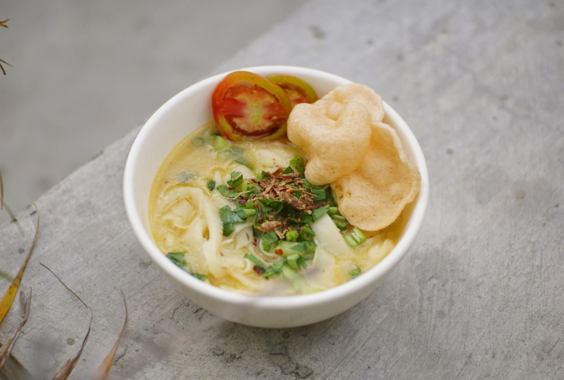 A bowl of turmeric-yellow Indonesian soto topped with fried shallots and a prawn cracker