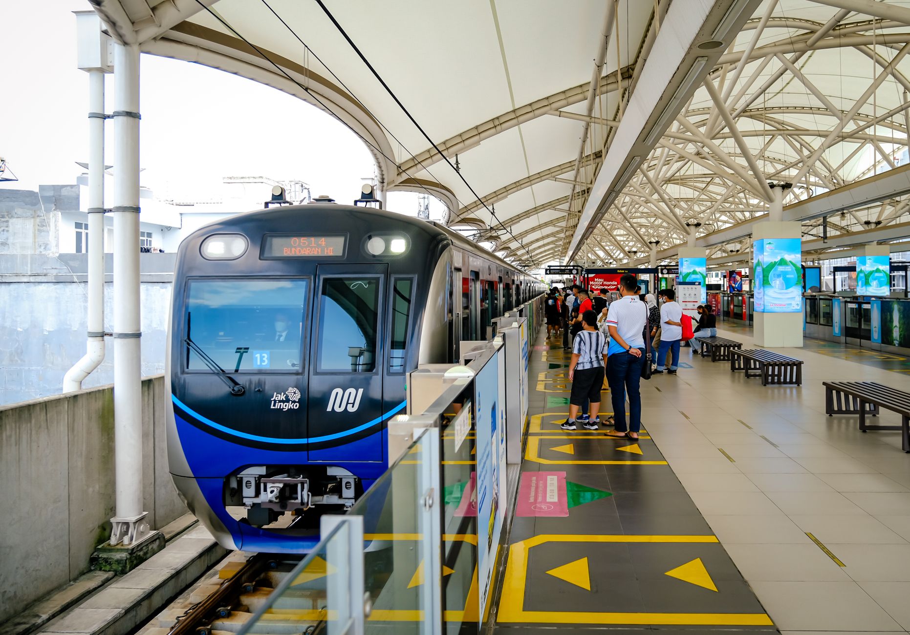 A blue Jakarta MRT train stopped at a platform with waiting commuters and platform markings