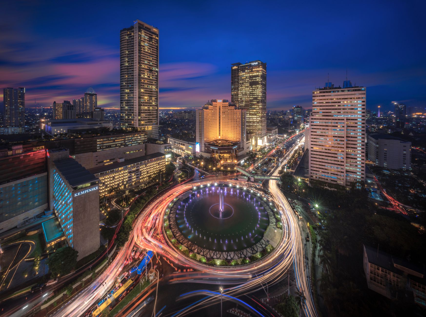 Aerial view of the Bundaran HI roundabout and Thamrin office towers lit up at dusk in Central Jakarta