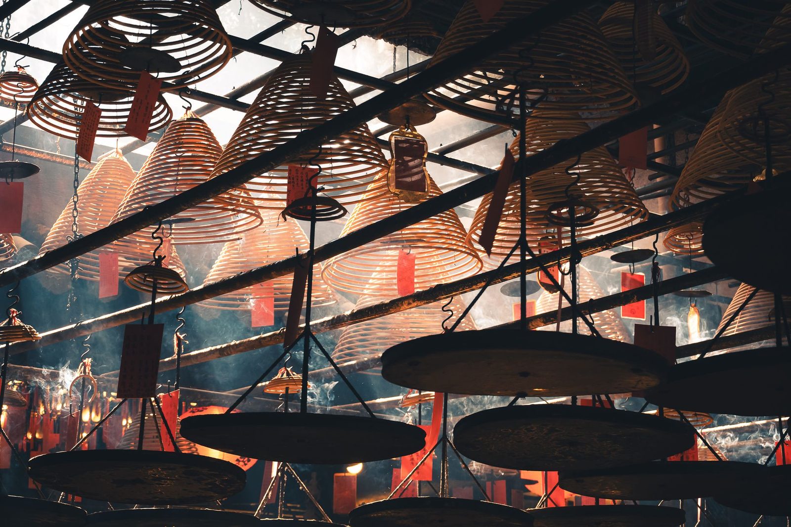 Spiral incense coils hanging from a temple ceiling with smoke and red candles below, as at Vihara Dharma Bhakti in Glodok