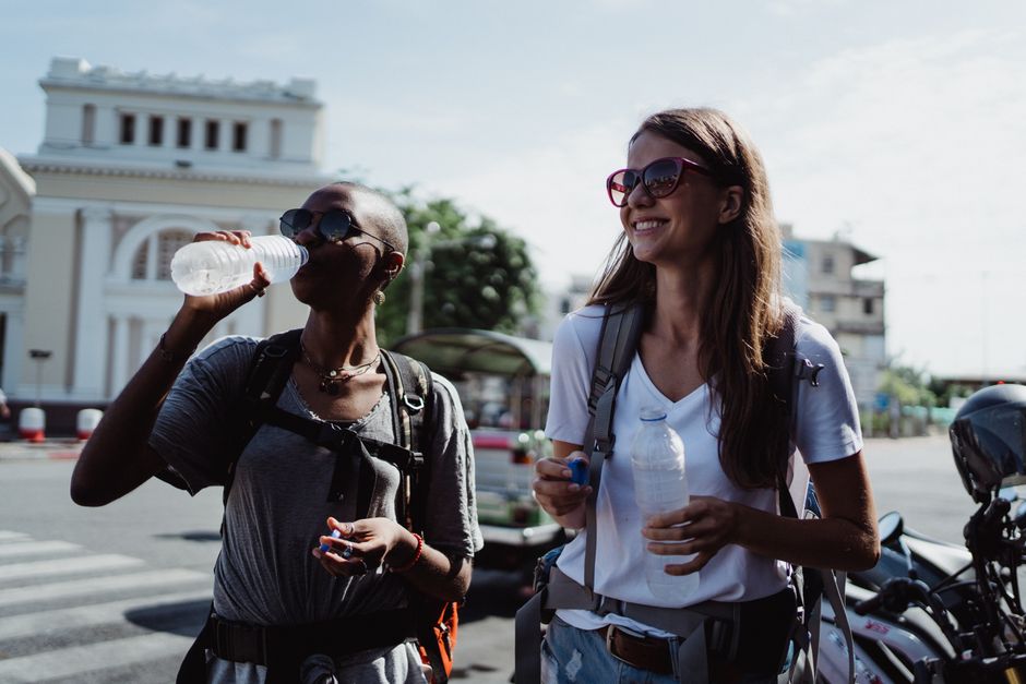 Two travellers drinking bottled water on a busy Southeast Asian street, a basic health precaution in Jakarta