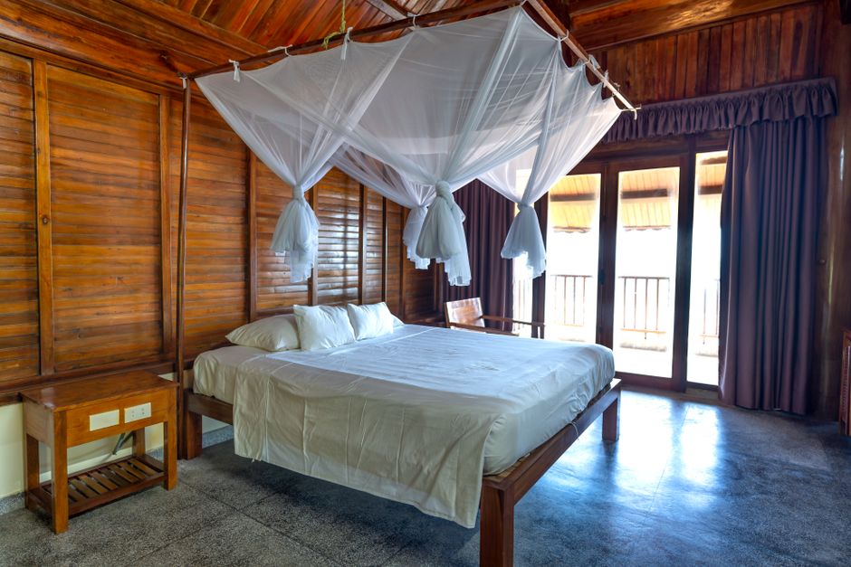 Mosquito net draped over a bed in a tropical wooden guesthouse room, a practical dengue prevention measure