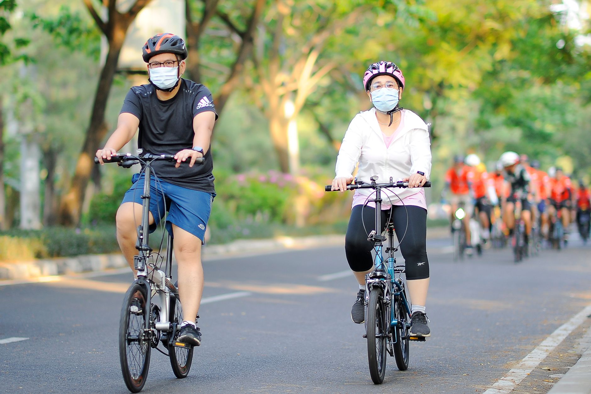 Two cyclists wearing face masks while riding on a tree-lined Jakarta road during car-free hours