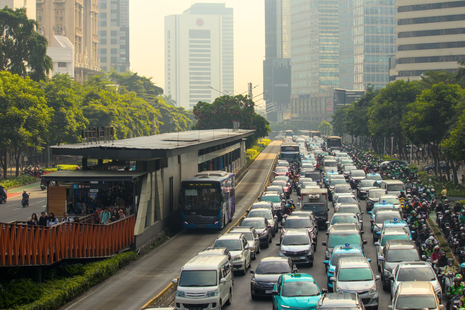 Heavy motorbike and car traffic on a Jakarta road with a visible haze layer over the skyline behind