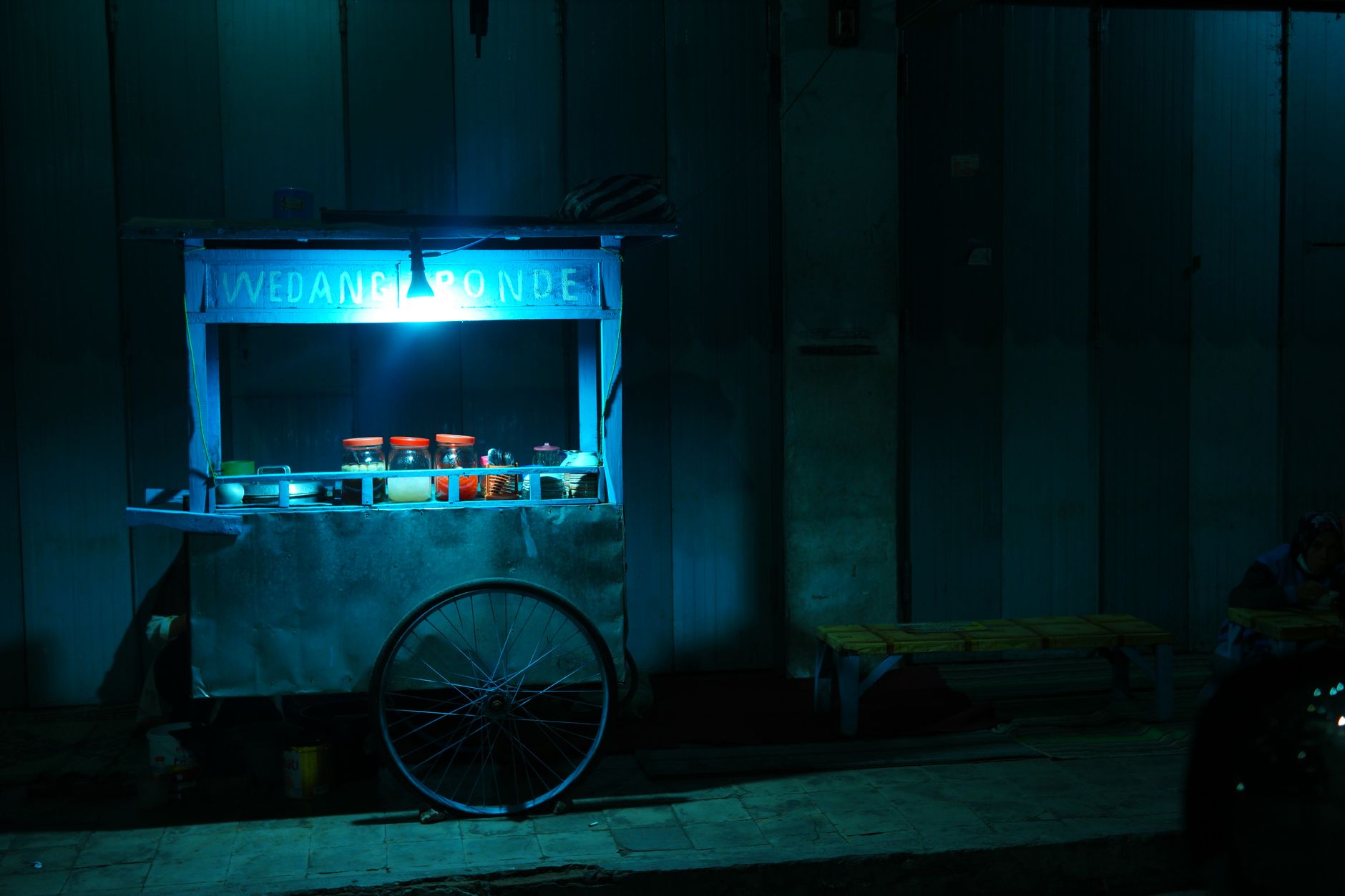 Lit food cart serving wedang ronde on a Jakarta street late at night