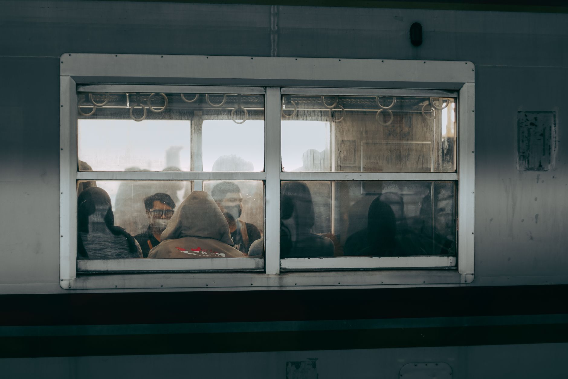 Passengers seen through the window of a crowded Jakarta commuter train at dusk