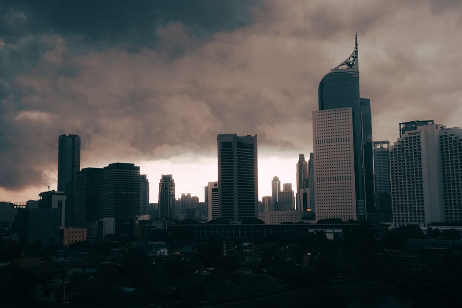 Jakarta city skyline with skyscrapers lit at dusk under a dramatic sky
