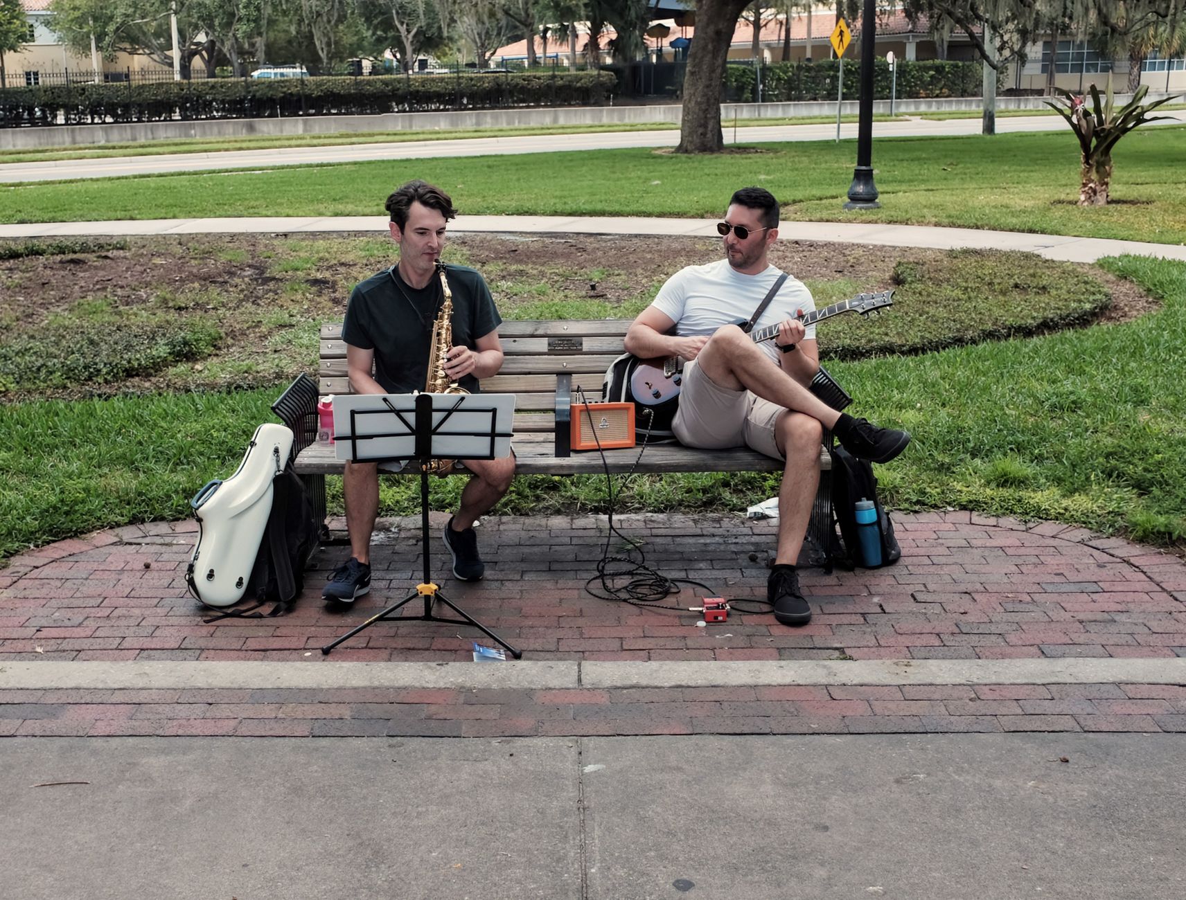 Two musicians with instruments seated in a leafy city park, a common Sunday sight in Menteng