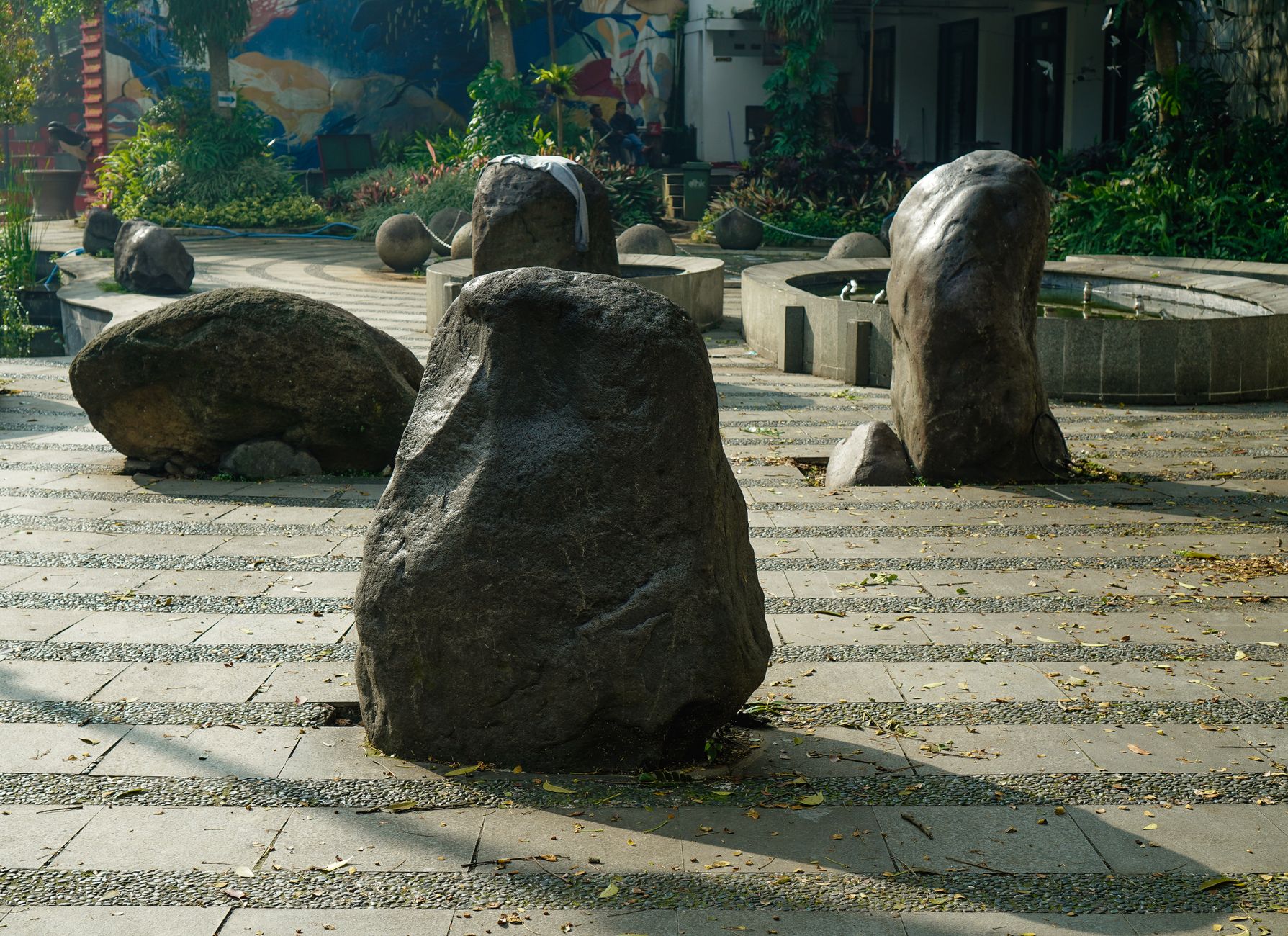 Stone sculptures on paving in a shaded Jakarta park, as at Taman Suropati in Menteng