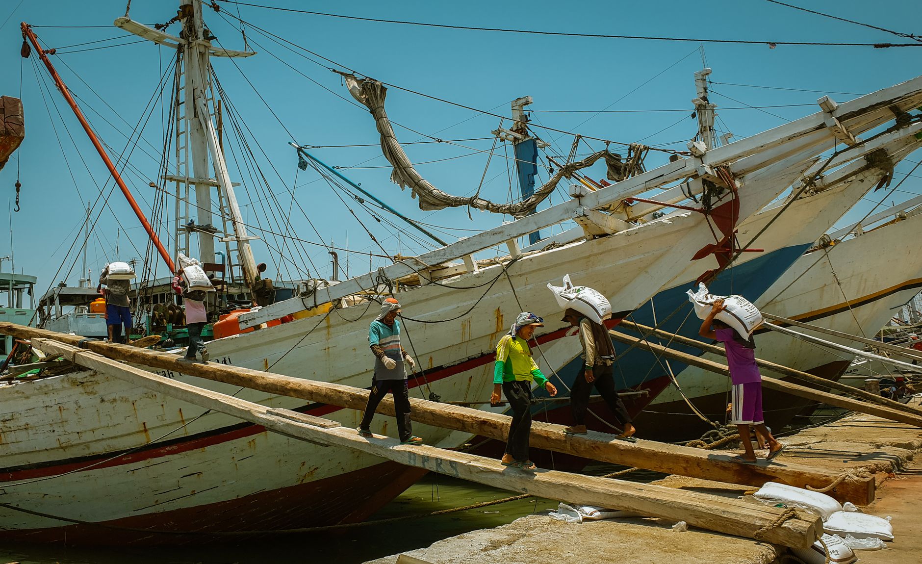 Wooden pinisi schooners moored at Sunda Kelapa with dockworkers on the gangplanks, a highlight of any North Jakarta Ancol guide