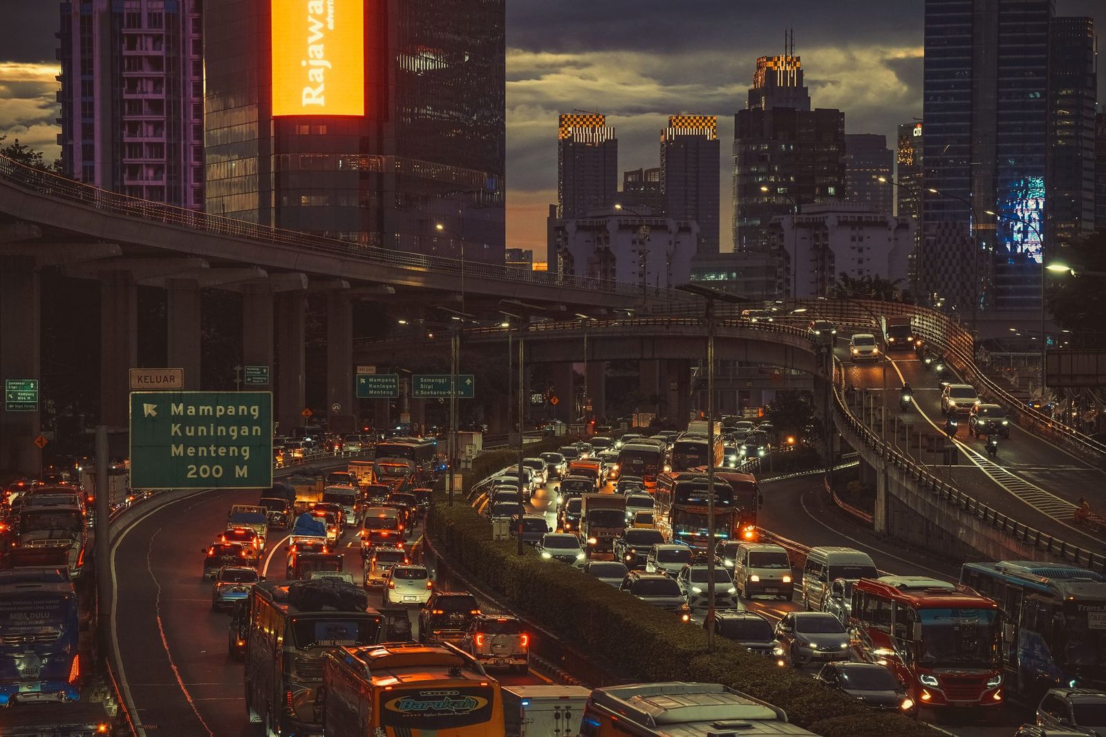 Heavy traffic on a Jakarta road at dusk with signage and lit towers, the daily reality around Pondok Indah