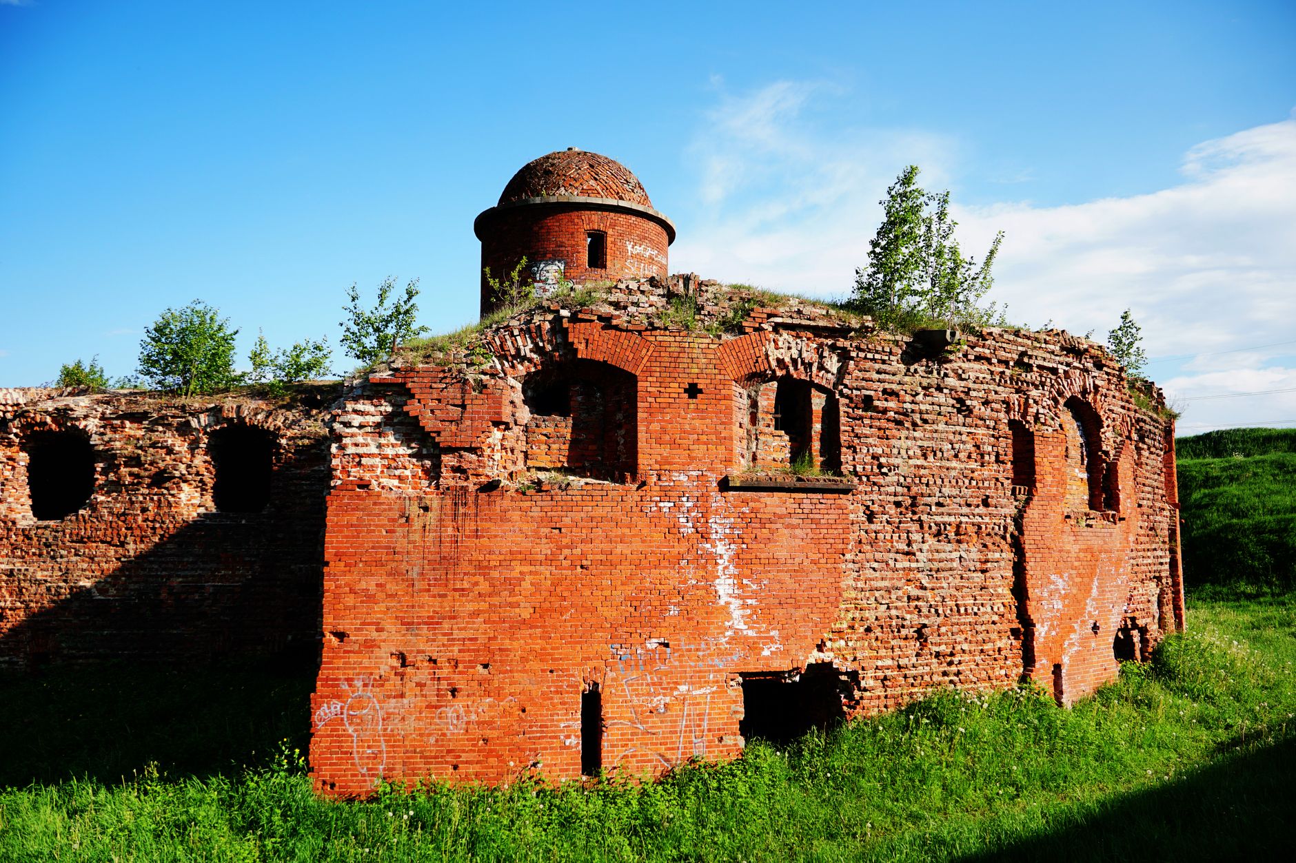 The overgrown remains of a circular red brick fort with grass growing from its walls