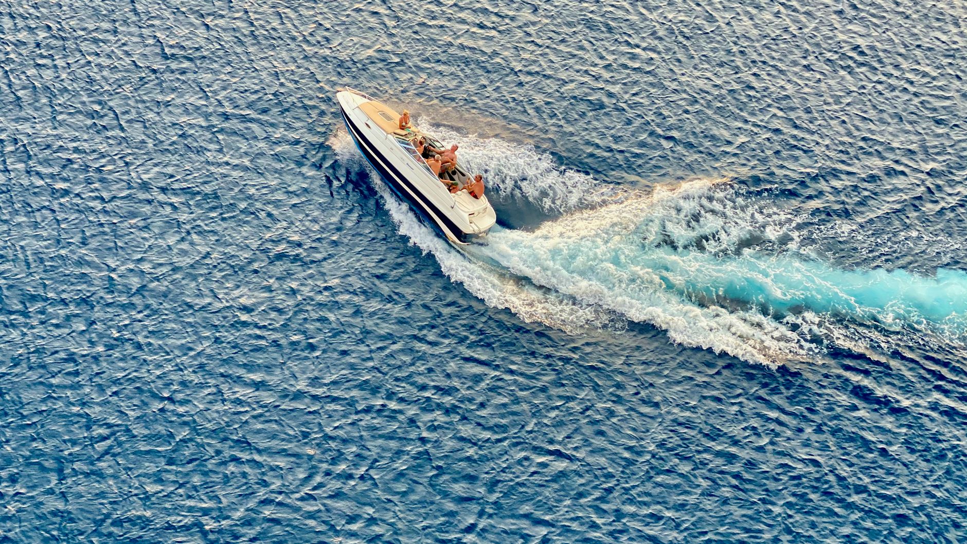 A speedboat cutting a white wake across deep blue open water
