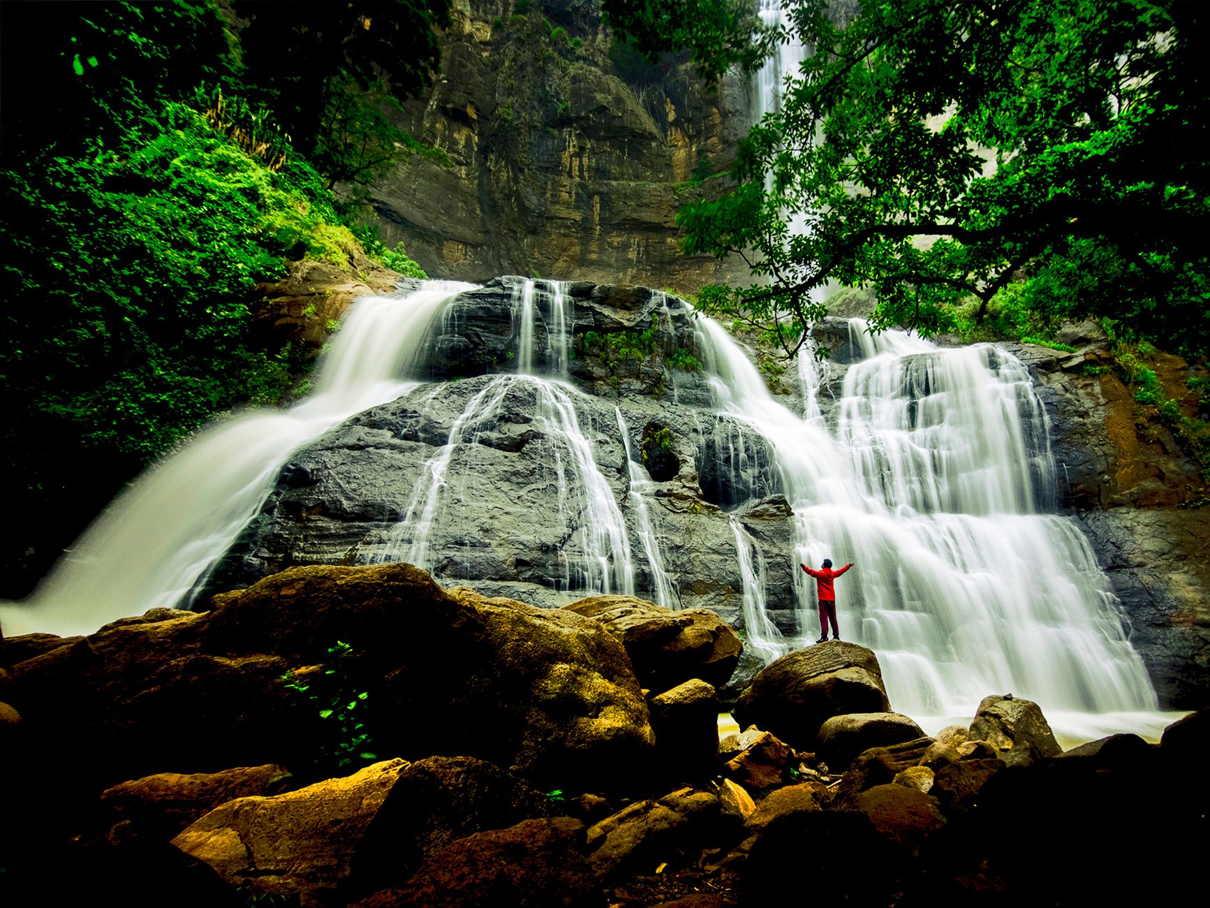 A wide waterfall falling into a rock pool surrounded by dense West Java forest