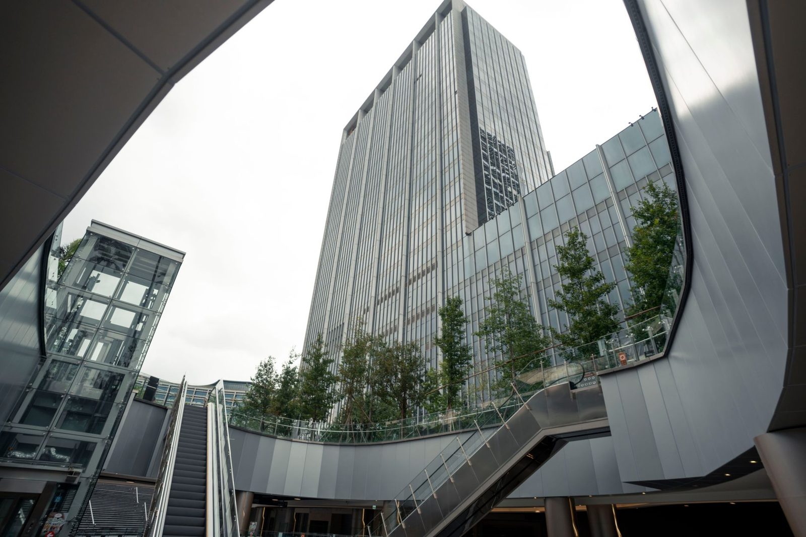A glass office tower with escalators and planting at a landscaped plaza in the SCBD estate, Jakarta
