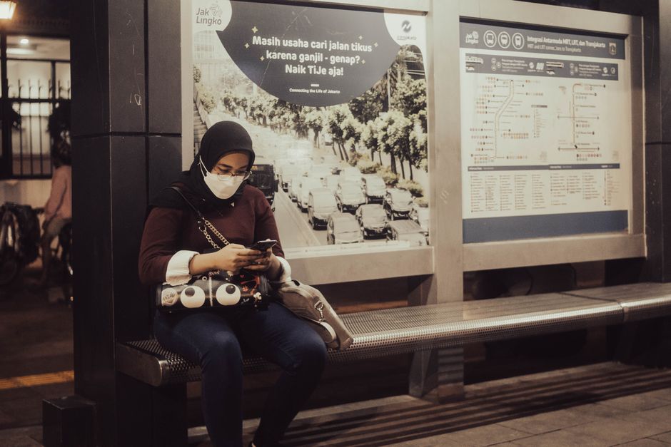 Woman using a smartphone at a Jakarta transit stop, relying on a local data connection to check routes