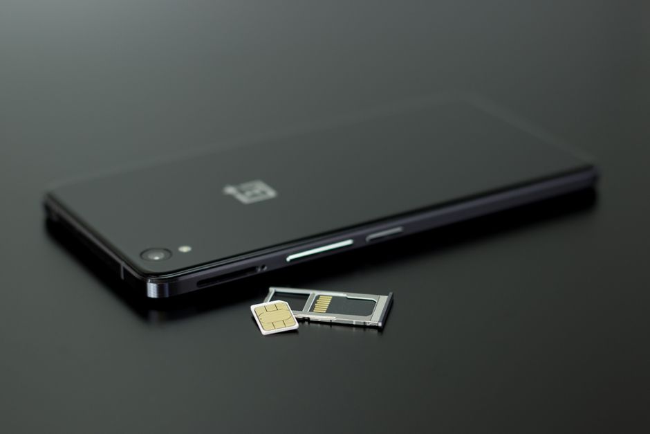 A physical SIM card and ejector tool next to a smartphone, illustrating the swap needed for a local Indonesian SIM