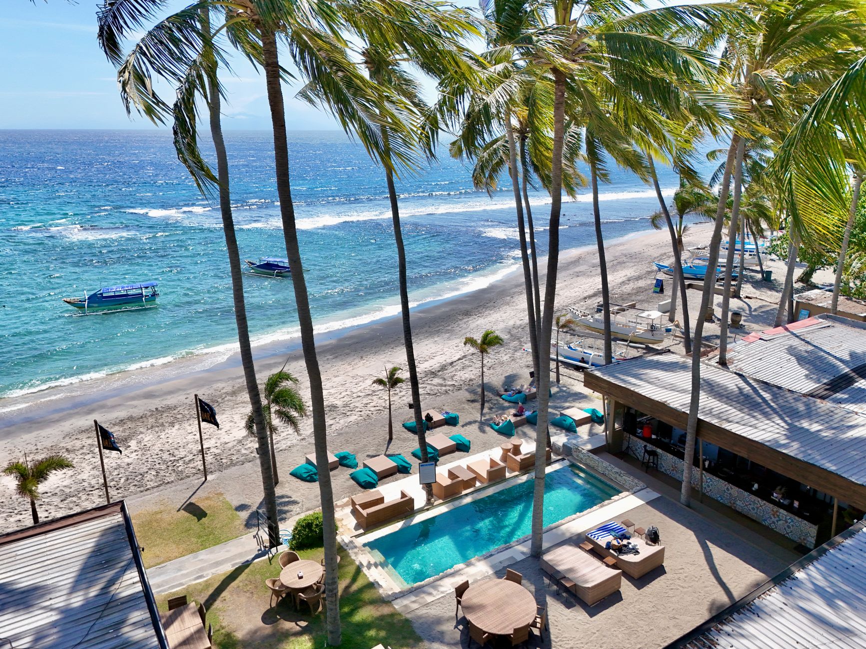 A resort pool and loungers set above a palm-fringed beach