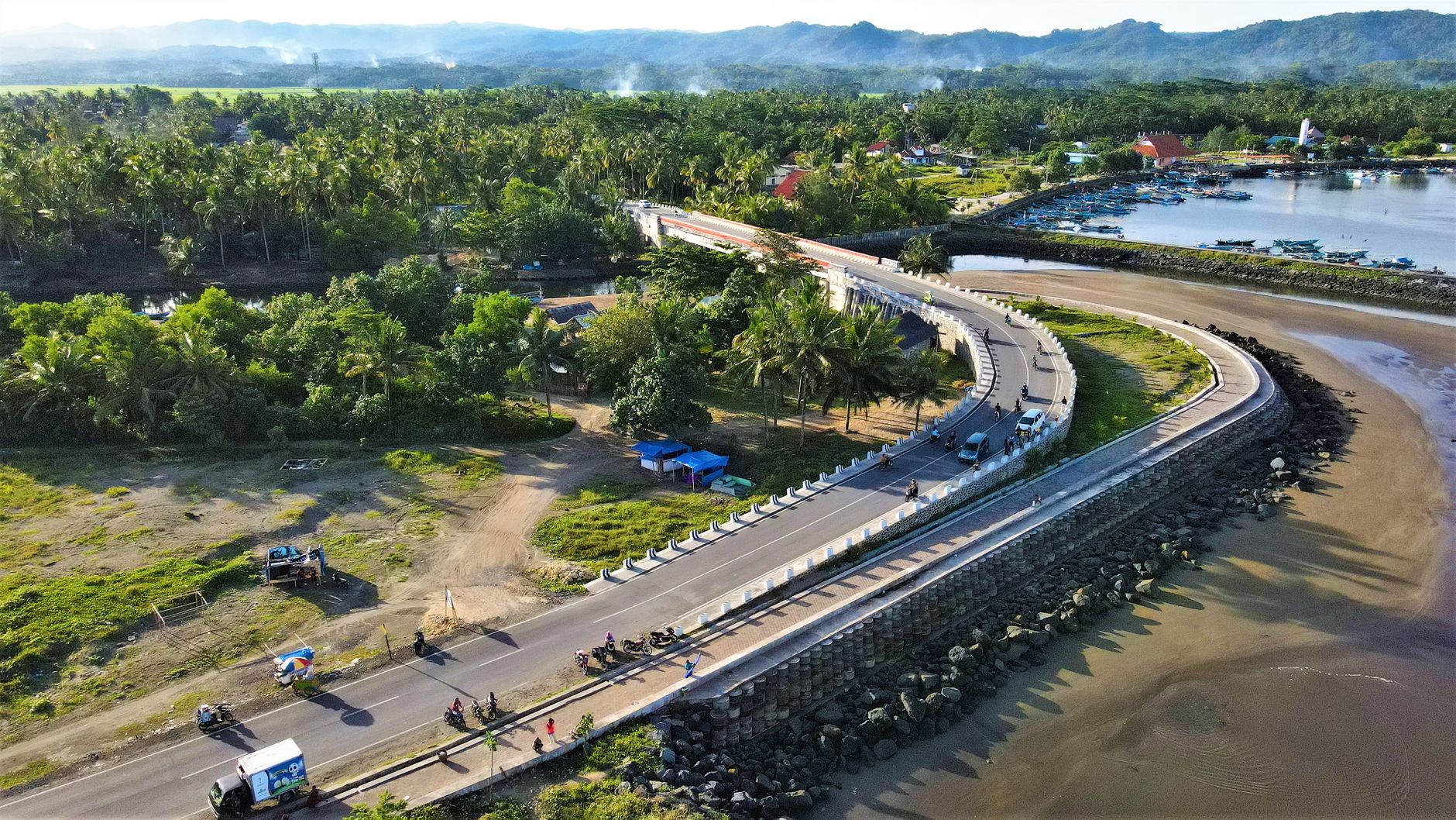 Aerial view of a coastal road running behind a seawall through a green village in western Java