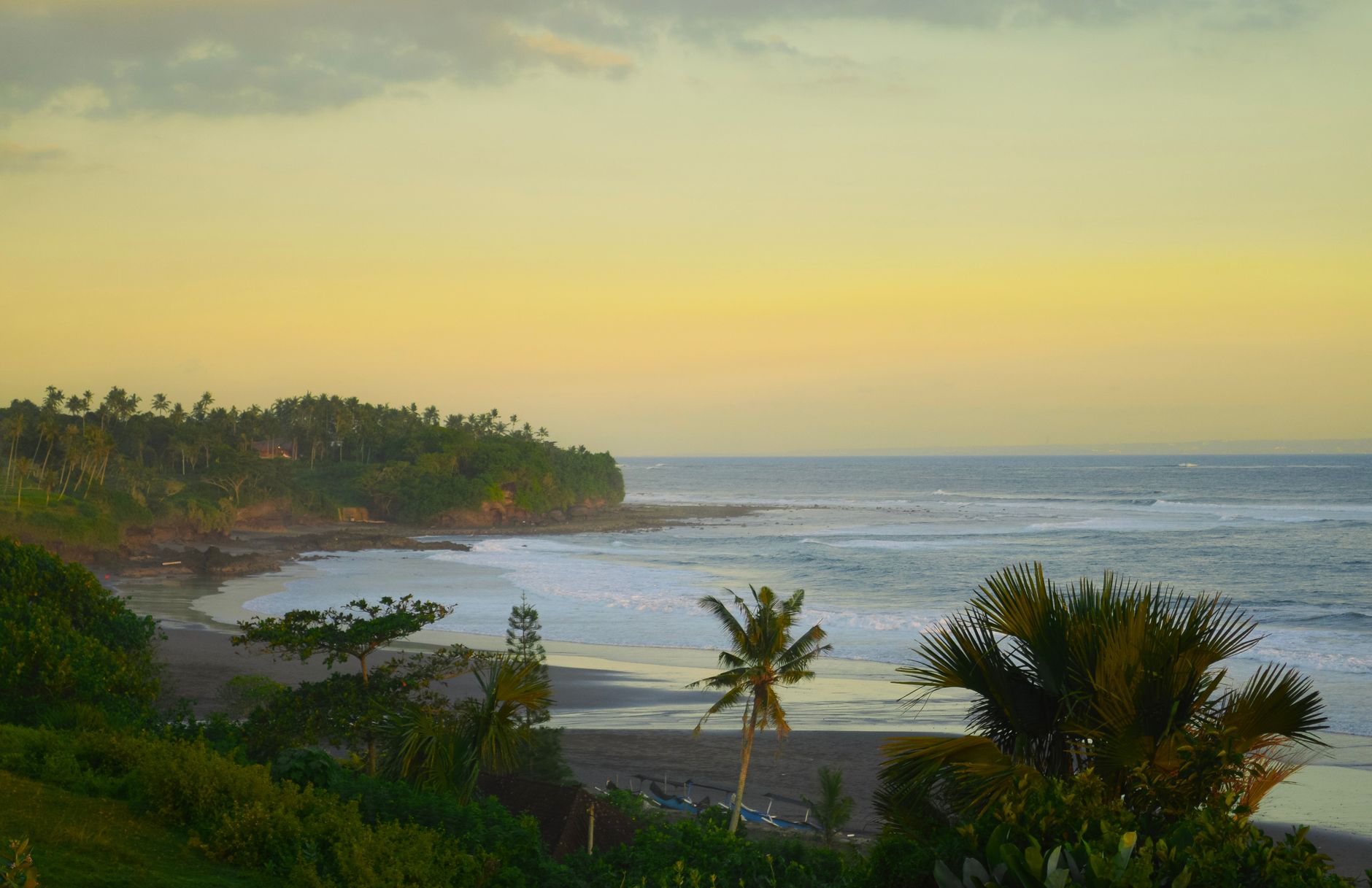 Palm trees silhouetted against a yellow sunset over the sea at a west-facing beach, the appeal of Tanjung Lesung beach from Jakarta