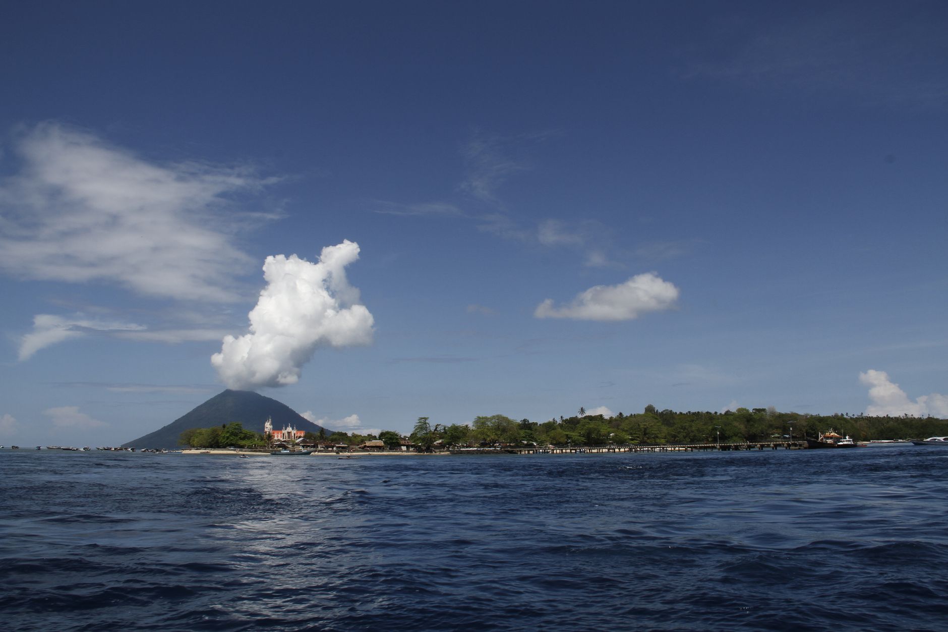 A conical volcanic island rising from calm sea under a clear sky