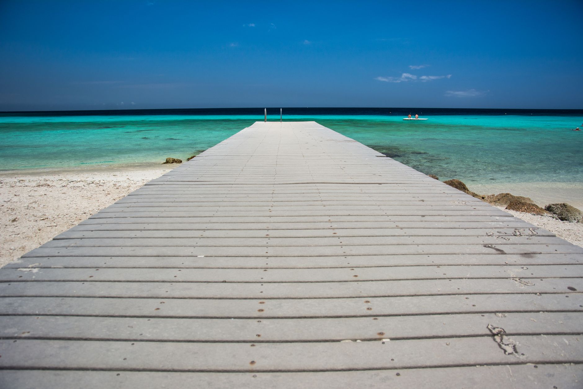 A concrete jetty running out from white sand into shallow turquoise water in the Thousand Islands near Jakarta