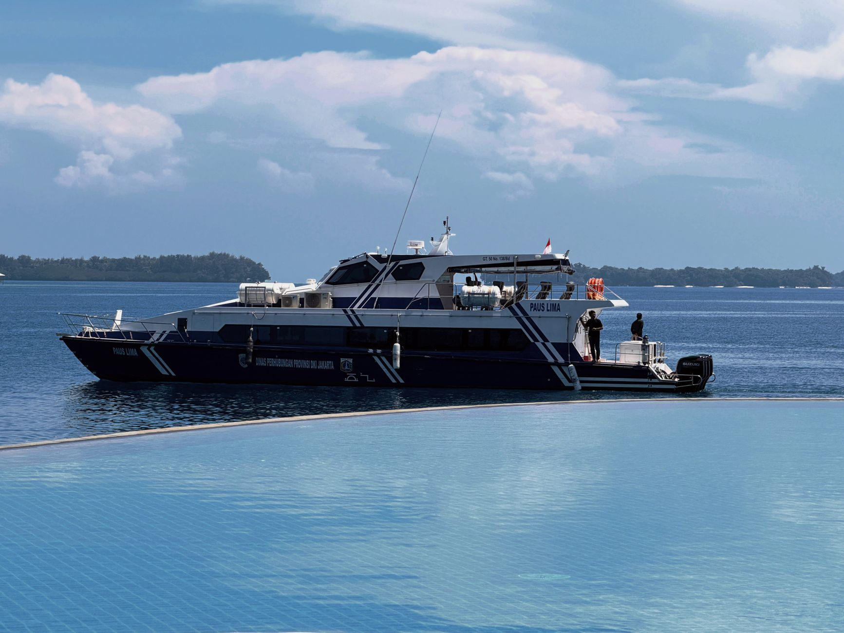 A passenger boat lying off a low tropical shoreline on the Jakarta coast