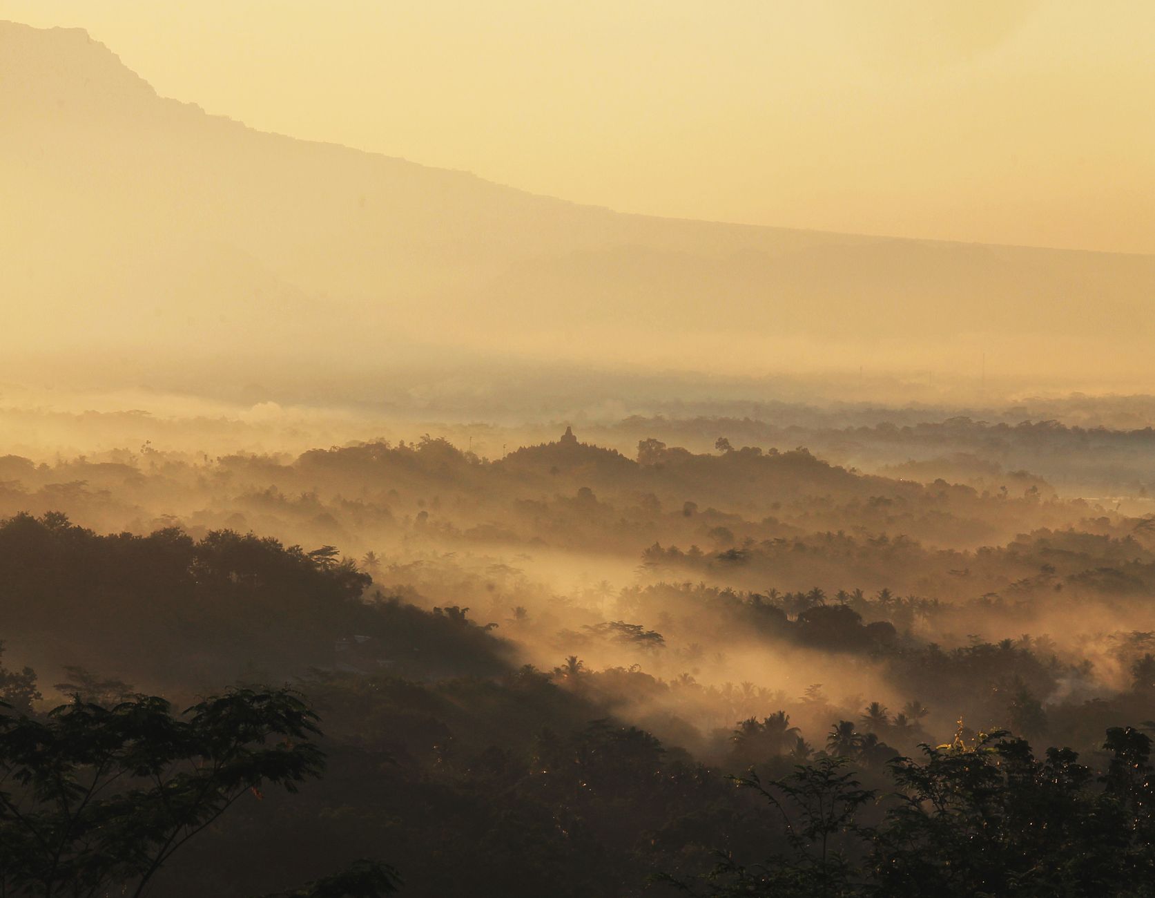 Golden sunrise light spreading over layered misty ridges and forest, the reward of weekend getaways near Jakarta