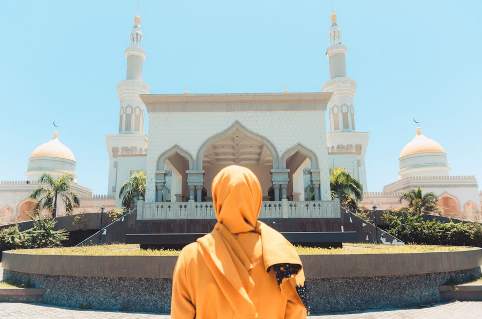 Woman in a modest long-sleeved outfit and headscarf standing before a mosque, as required for Istiqlal Mosque visits