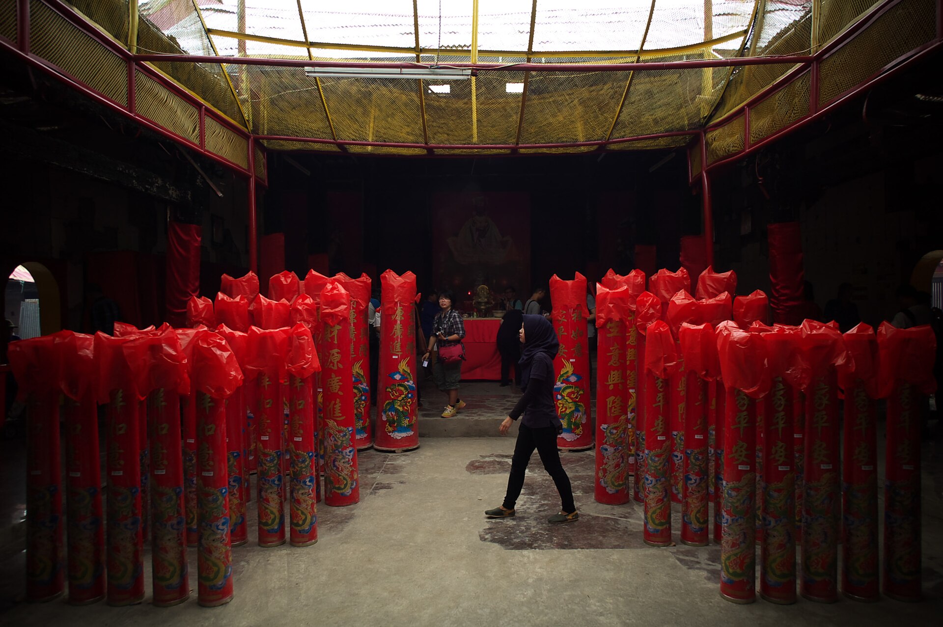 A visitor in a headscarf walks between rows of giant red candles decorated with gold Chinese characters and dragons inside a temple at Petak Sembilan, Glodok