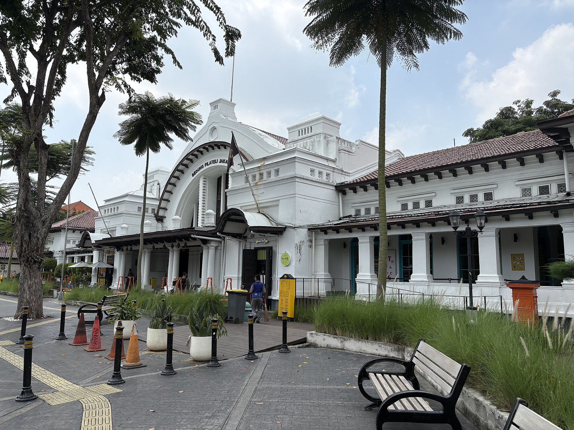 The white colonial facade of the Gedung Filateli, the old post office that now houses Pos Bloc, with its arched entrance, palm trees and benches on the pavement outside