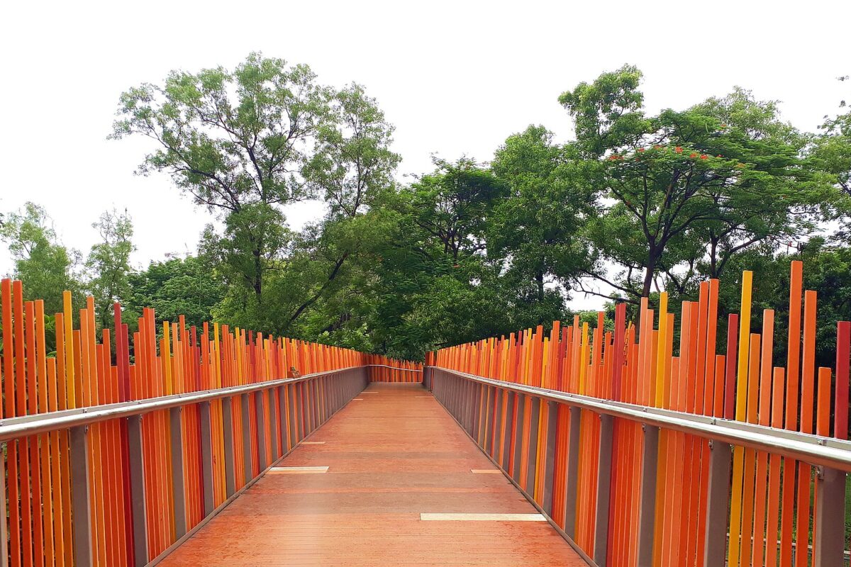 The orange slatted Infinity Link Bridge walkway curving between trees at Tebet Eco Park in South Jakarta