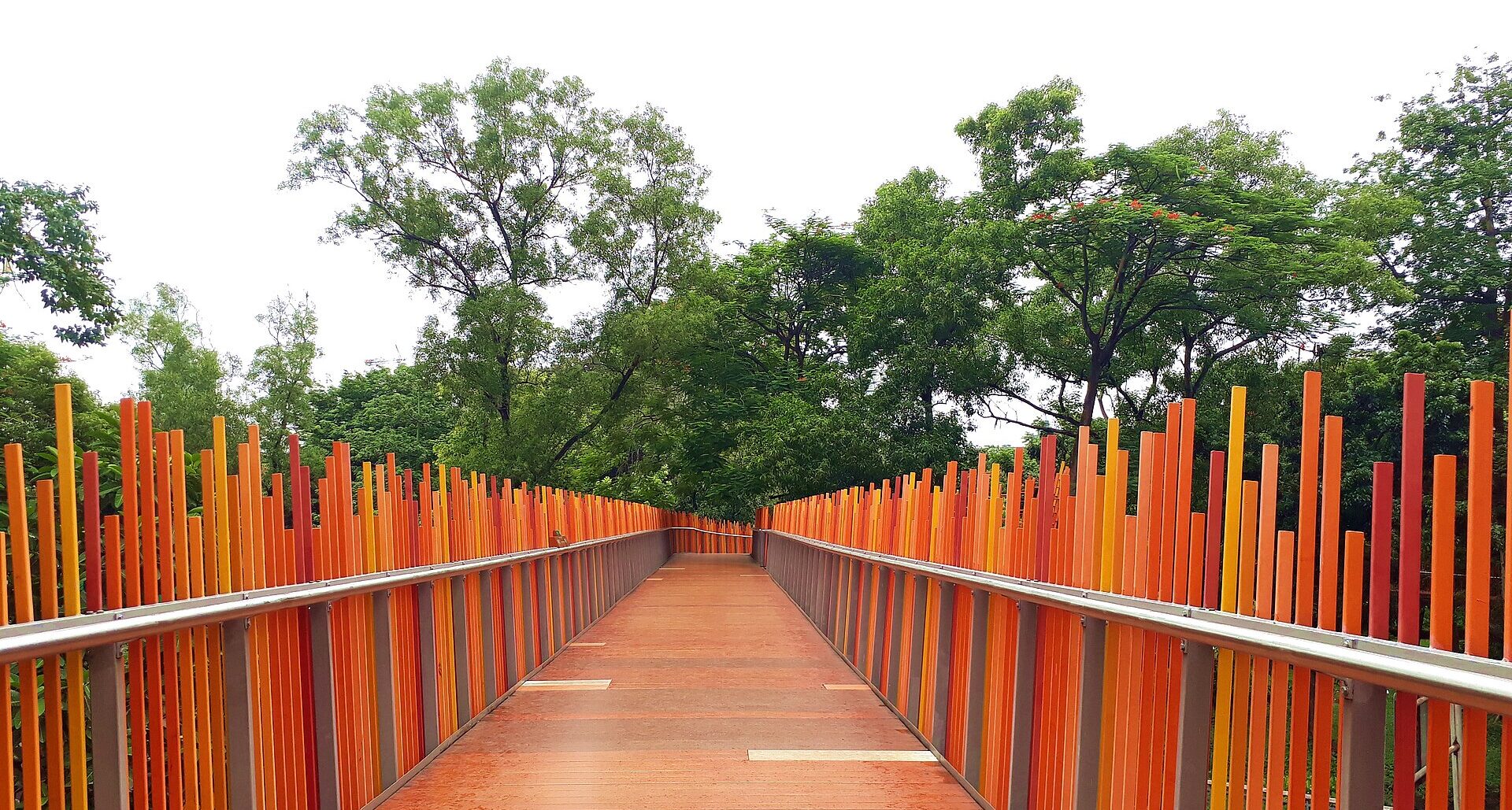 The orange slatted Infinity Link Bridge walkway curving between trees at Tebet Eco Park in South Jakarta